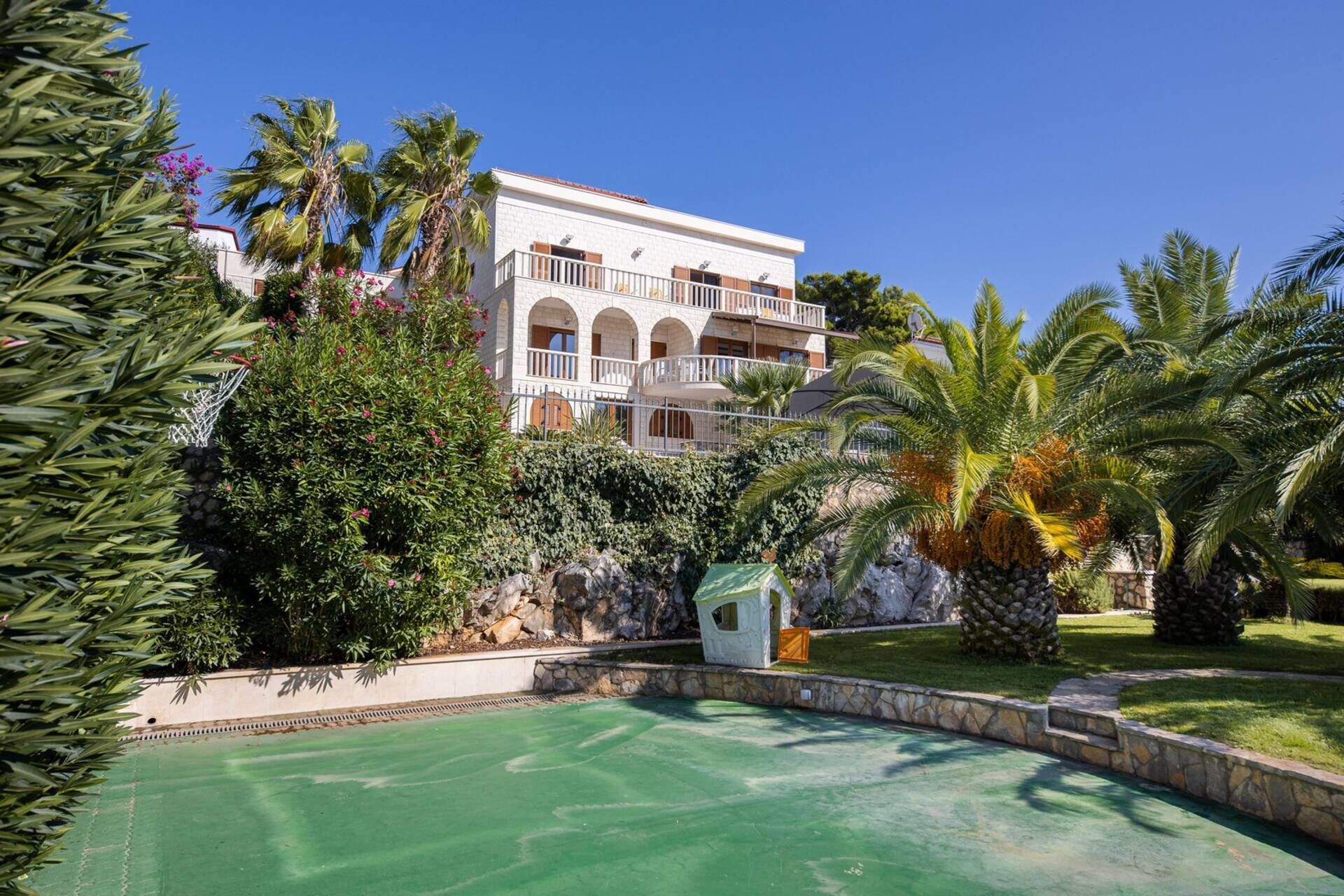 Ein Hotel mit Schwimmbad, umgeben von Palmen und viel Grün.