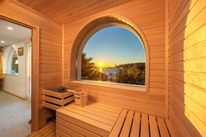 Relax in a serene sauna with a stunning view of the coastal landscape through the large arched window.