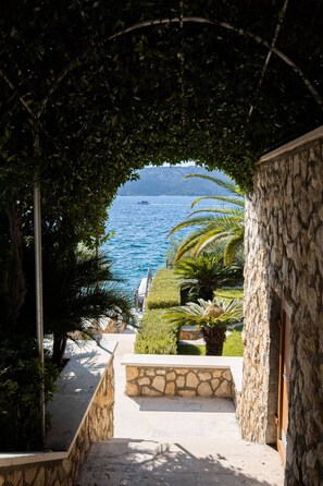 Stroll along the pathway to a serene coastal view, flanked by lush hedges and palm trees.