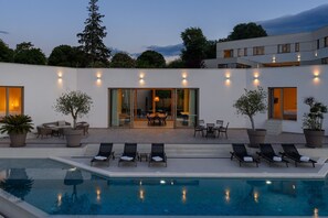 A modern poolside area with lounge chairs, a dining area, and a large window overlooking the pool.