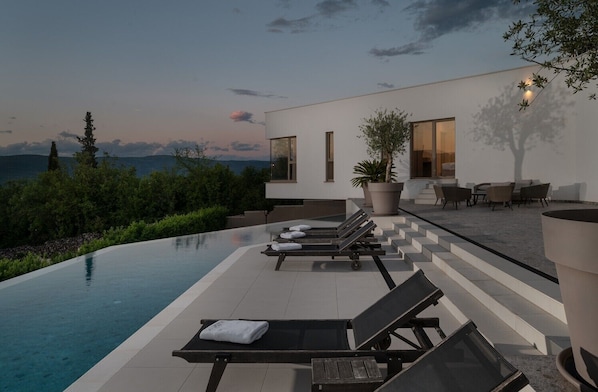 A modern outdoor pool area with lounge chairs, a potted plant, and a view of the mountains.
