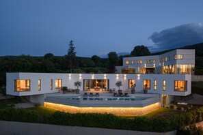 A modern two-story house with a swimming pool, outdoor seating, and a stone wall.
