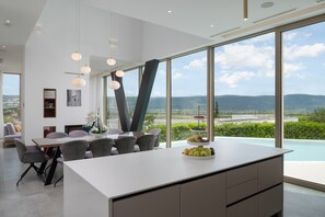A modern kitchen with a central island, dining area with chairs, and large windows offering a view of the landscape.