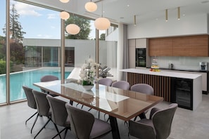 Une cuisine moderne dotée d’un îlot central, d’un coin repas avec une table en verre et d’une vue sur une piscine.