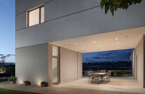 Un bâtiment moderne doté d’un patio comprenant une table et des chaises, une porte vitrée et offrant une vue sur la ville la nuit.