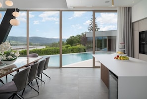 A modern kitchen with a large island, a dining area with chairs, and a view of a swimming pool and mountains.