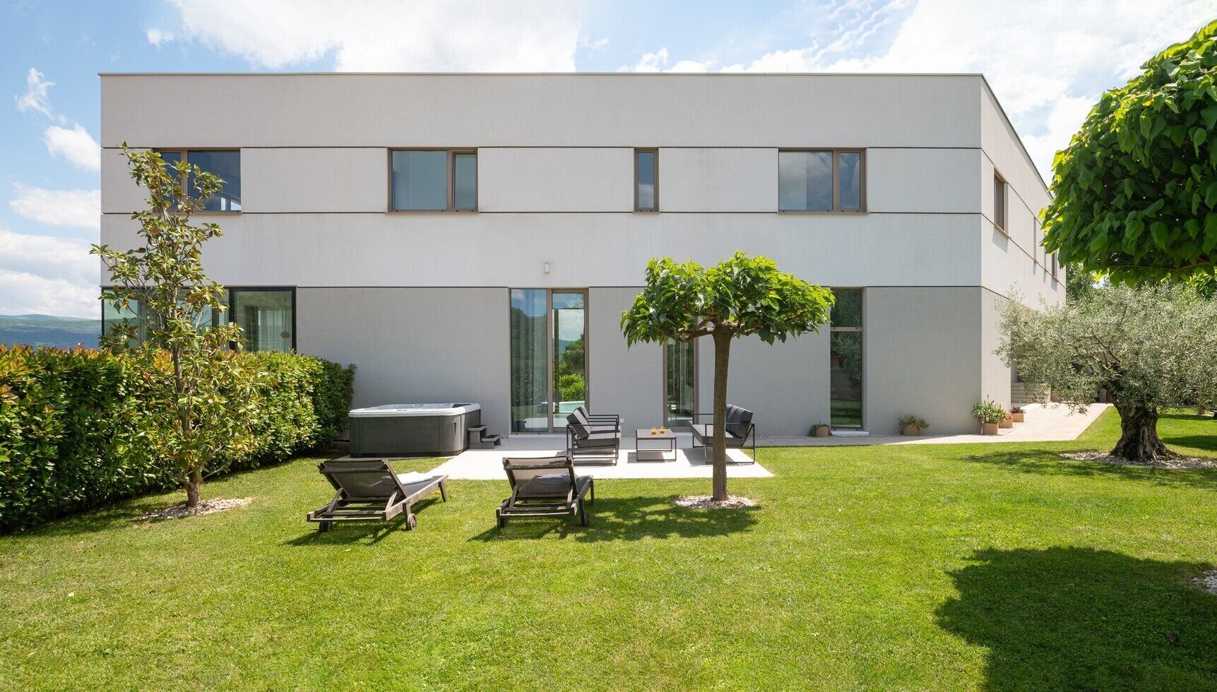 A modern two-story building with a flat roof, large windows, and a well-maintained lawn with outdoor furniture.