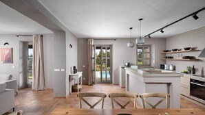 A modern kitchen with a central island, a dining area with a wooden table, and a view of a pool through an open door. - Rustic Villa Rubus with a pool in Istri, panoramic view, pet friendly (Sveti Lovrec)