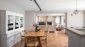 A spacious living area with a wooden dining table, cushioned chairs, a stone fireplace, and a modern kitchen with white cabinetry. - Rustic Villa Ruta with a pool in Istri, panoramic view, pet friendly, quite area, family, private parking, terrace, fancy yard (Sveti Lovrec)