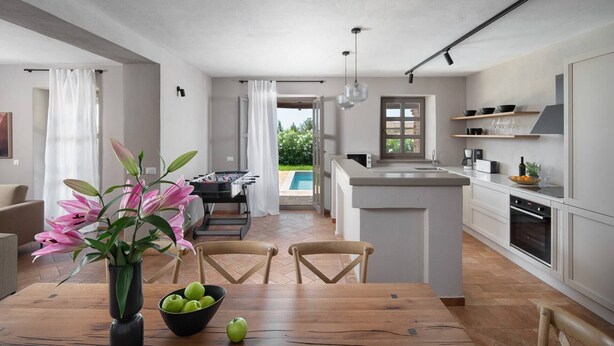 A modern kitchen with a central island, a dining area with a wooden table and chairs, and a visible outdoor pool area. - Rustic Villa Ruta with a pool in Istri, panoramic view, pet friendly, quite area, family, private parking, terrace, fancy yard (Sveti Lovrec)