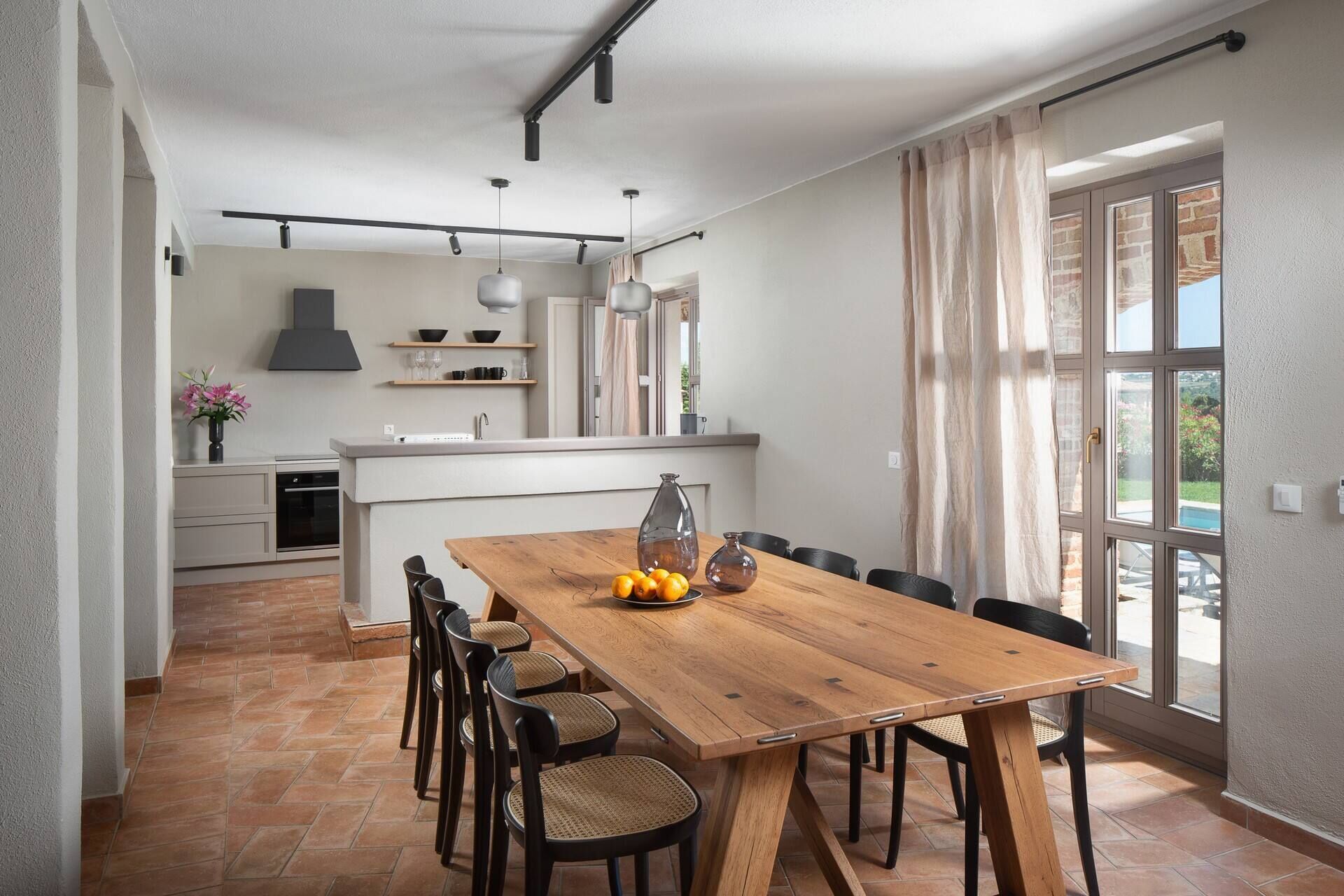 Una cocina amplia con una isla central, un comedor con mesa y sillas de madera, y un gran ventanal con cortinas.
