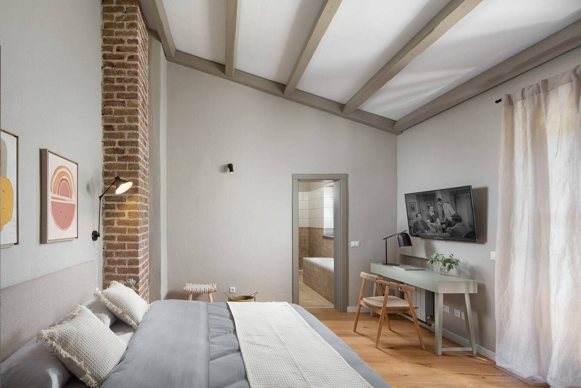 A modern bedroom with a bed, a desk, and a TV.