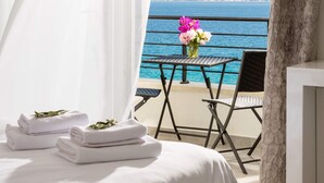 Ein Schlafzimmer mit Bett, einem kleinen Tisch mit Blumenvase und einem Balkon mit Meerblick.