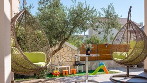 A patio with two hanging chairs, a small table, and a children's play area.