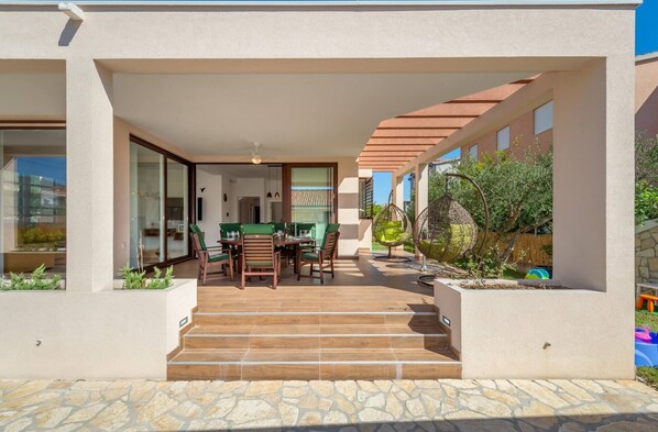 A modern house with a covered patio, a dining area, and a stone-tiled entrance.