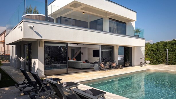 A modern two-story house with a swimming pool, glass doors, and outdoor seating.