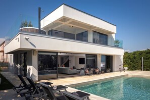 A modern two-story house with a swimming pool, glass doors, and outdoor seating.