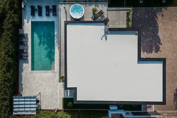 An aerial view of a modern pool area with a rectangular pool, a hot tub, and a seating area with chairs and tables.