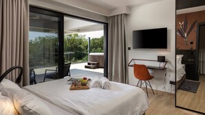 A modern hotel room with a large bed, a desk with a chair, a TV mounted on the wall, and a balcony with a hot tub.
