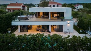 A modern two-story house with a glass balcony, a hot tub, and a bicycle.