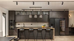 A modern kitchen with dark cabinetry, a central island with bar stools, and a built-in wine cooler.