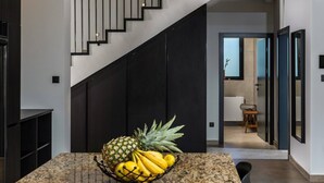 A modern kitchen with a granite countertop, a fruit bowl containing pineapple, bananas, and lemons, and a staircase leading to another room.