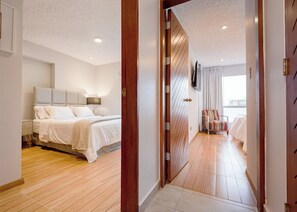 Ein Hotelzimmer mit Bett, Nachttisch, Lampe und Blick auf den Flur.
