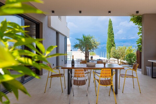 Une terrasse extérieure avec une table et des chaises, une bouteille de champagne et une vue sur la mer.