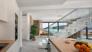 Et moderne køkken med en glaskonstrueret trappe, der fører op til en balkon med udsigt over vandet.
