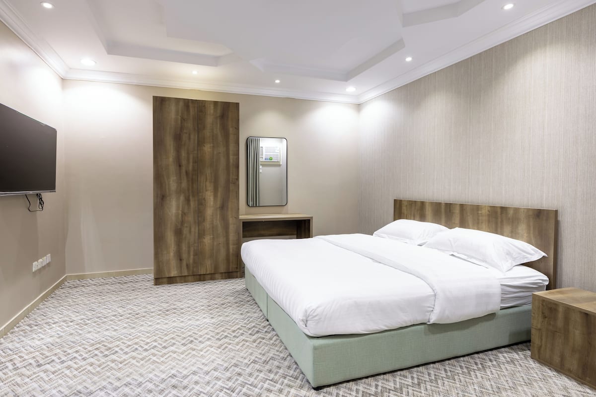 Une chambre d’hôtel moderne avec un grand lit, une tête de lit en bois, un téléviseur intégré et une petite table de chevet.