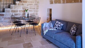 A stone-walled room with a curved staircase, a round table with chairs, and a sofa. - Casa di Recente Ristrutturazione, in Locazione Turistica, a due Passi dal Mare (Puglia)