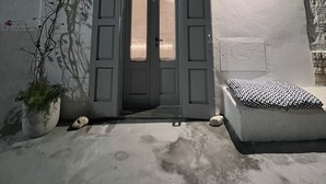A white building with a dark wooden door, a small round light above the door, and a potted plant with red flowers to the left. - Casa di Recente Ristrutturazione, in Locazione Turistica, a due Passi dal Mare (Puglia)