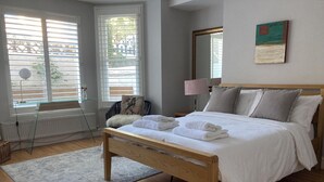 A neatly made bed with white linens and towels, a wooden headboard, and a large window with blinds. - Garden flat in central Hove, close to the beach, shops, bars and restaurants (Brighton and Hove)