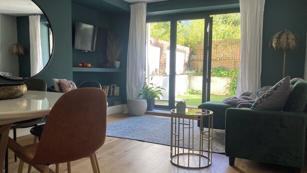 A modern living room with a dining area, a large mirror, and a view of the garden through glass doors. - Garden flat in central Hove, close to the beach, shops, bars and restaurants (Brighton and Hove)