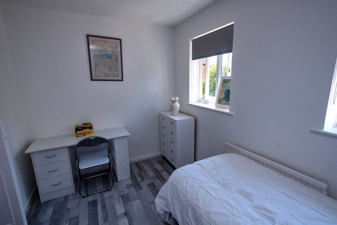 Un dormitorio con cama, escritorio, silla, cómoda y ventana con persianas.