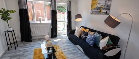 A modern living room with a black sofa, a coffee table, a floor lamp, and a painting on the wall.