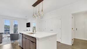 Una cocina moderna con una isla grande, muebles blancos e iluminación colgante.