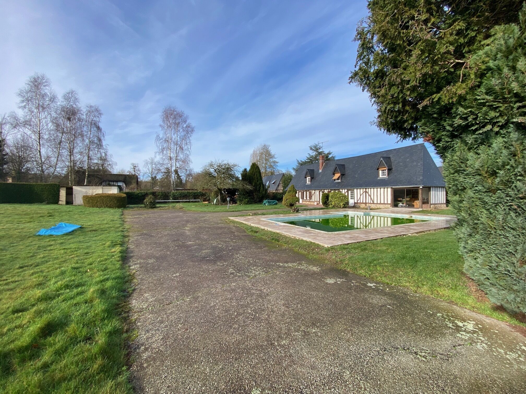 A residential property with a gravel driveway, a swimming pool, and a large lawn.