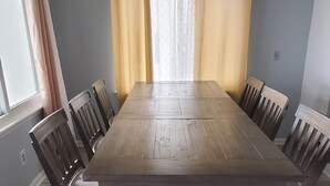 Ein Esszimmer mit einem langen Holztisch, Stühlen, einer Hängelampe und Vorhängen an den Fenstern.
