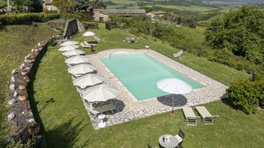 A swimming pool with lounge chairs and umbrellas, surrounded by stone walls and greenery. - Apartment Marcigliana Front Pool Radicondoli (Radicondoli)