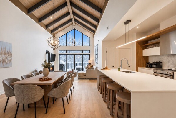A modern kitchen with a large island, bar stools, and a dining area with a wooden table and chairs.