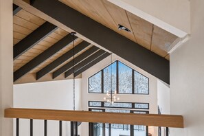 Ein Zimmer mit hohen Decken und freiliegenden Holzbalken, ein großes Fenster mit Blick auf schneebedeckte Bäume und eine hängende Leuchte.