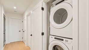 A laundry room with two stacked front-loading washing machines and a door leading to another room. - Tremblant Prestige - Verbier 14-202 (Mont-Tremblant)