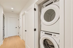A laundry room with two stacked front-loading washing machines and a door leading to another room. - Tremblant Prestige - Verbier 14-202 (Mont-Tremblant)