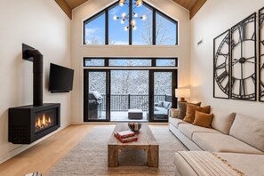 A modern living room with a fireplace, a sofa, a coffee table, and a large window overlooking a snowy landscape.