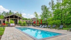 A rectangular swimming pool with lounge chairs and umbrellas, surrounded by a paved deck and a fence. - Tremblant Prestige - Verbier 14-202 (Mont-Tremblant)