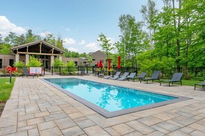 A rectangular swimming pool with lounge chairs and umbrellas, surrounded by a paved deck and a fence. - Tremblant Prestige - Verbier 14-202 (Mont-Tremblant)