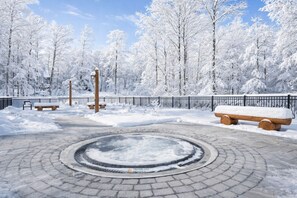 Een park bedekt met sneeuw, met een ronde fontein, banken en een hek.