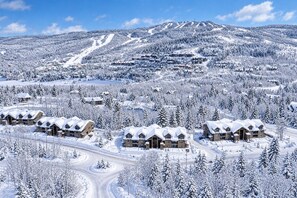 Ein schneebedecktes Bergresort mit mehreren Chalets, Skipisten und wolkenlosem Himmel.