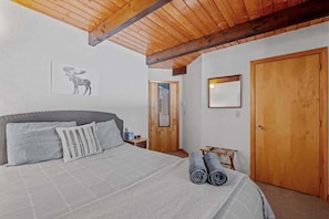 Un dormitorio con cama, almohadas, una obra de arte de un alce, una puerta de madera y una mesita.